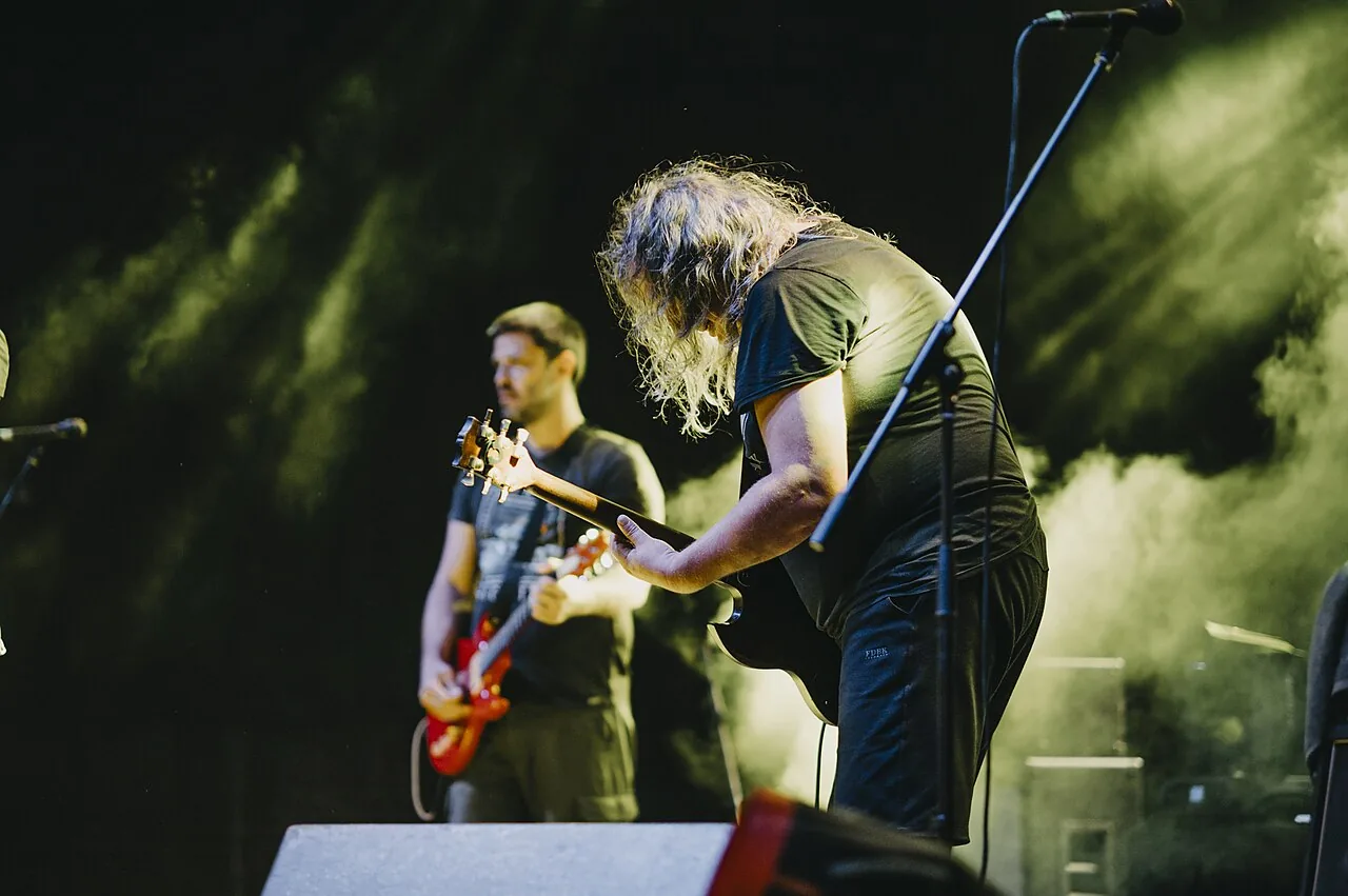 Live rock concert performance featuring musicians playing guitar on stage at night with vibrant lighting effects